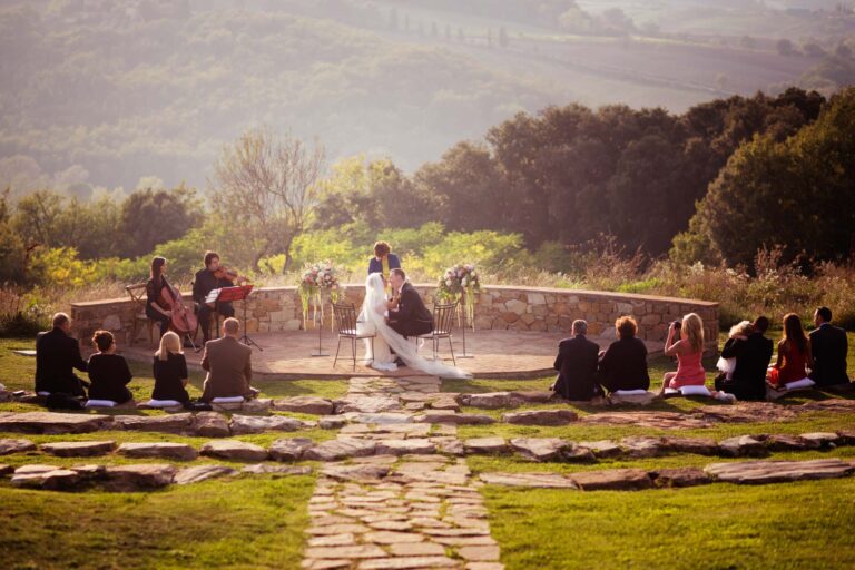 A ceremony on a stone terrace in the hills, guests seated on cushions, musicians to one side, Tuscan DMC
