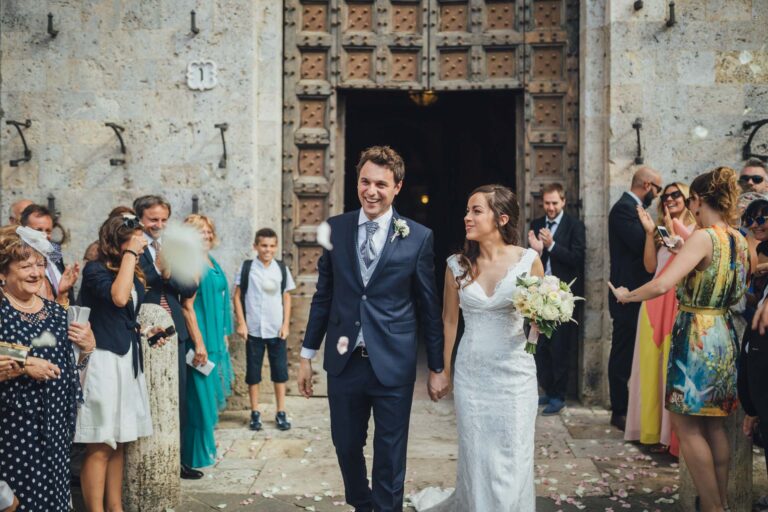 The couple leaving a church through a carved stone doorway to a crowd of guests, Tuscan DMC