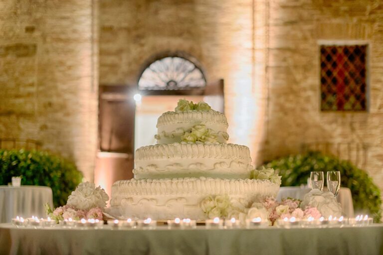 A tiered white wedding cake with sugar flowers on a candlelit table, Tuscan DMC