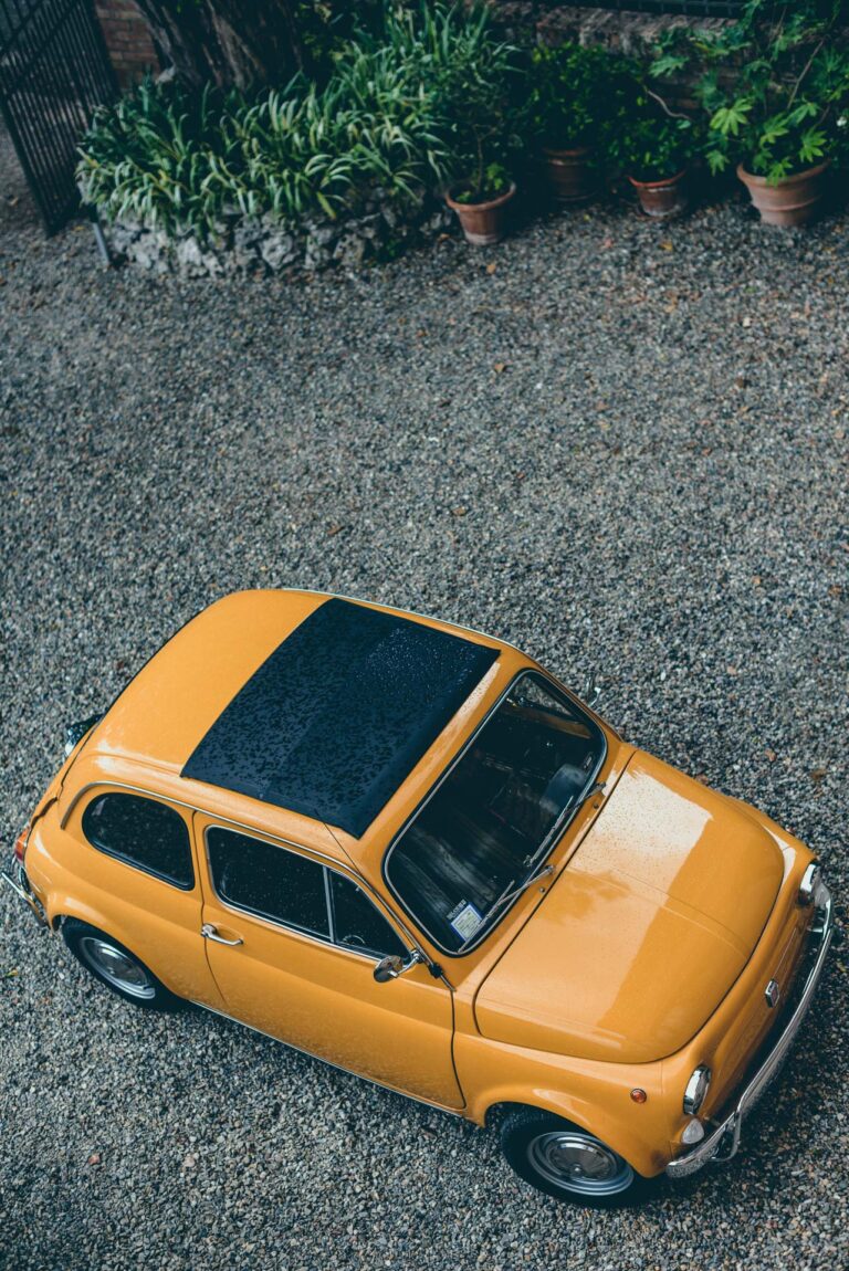 A vintage yellow Fiat 500 in a gravel courtyard, seen from above, Tuscan DMC