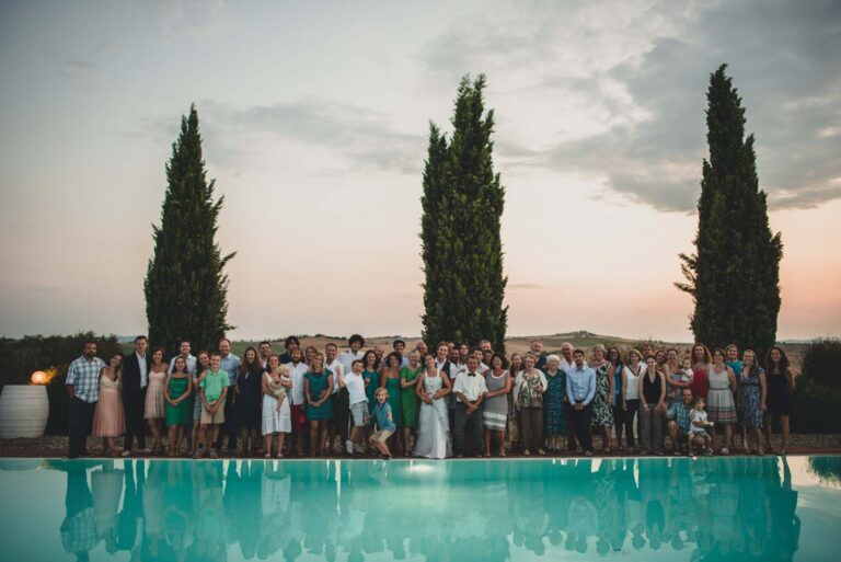 The wedding party lined up beside a pool at sunset, three cypresses behind, Tuscan DMC