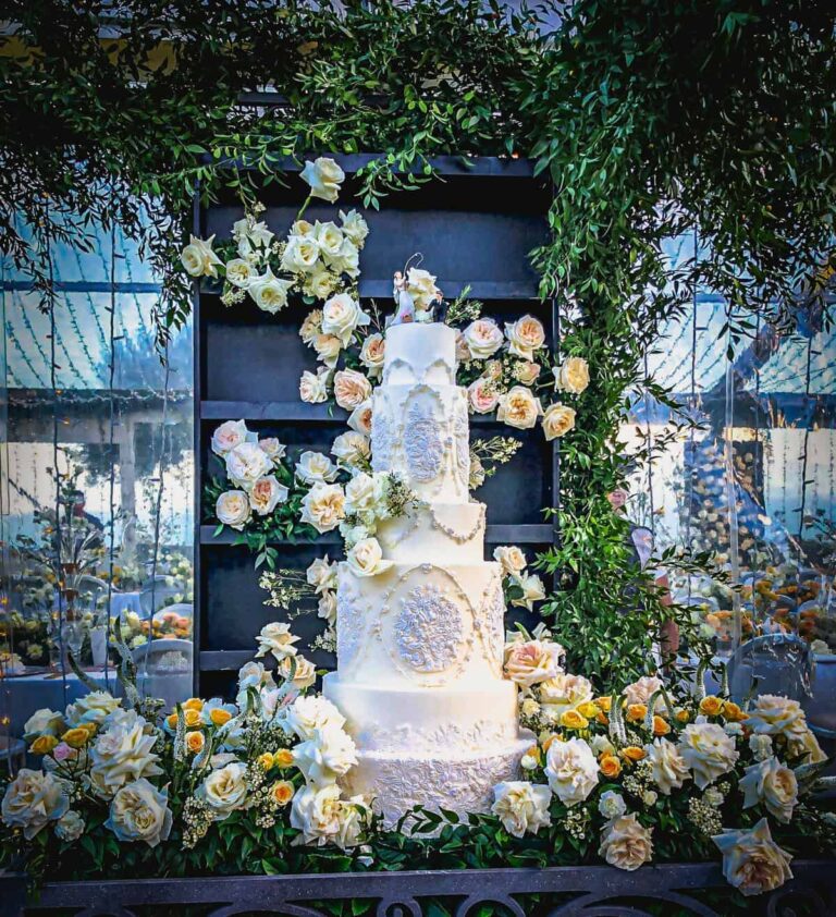 Monumental ivory tiered wedding cake with intricate piping and bas-relief medallion details, styled with roses and greenery at Villa Cimbrone in Ravello on the Amalfi Coast, Italy., Tuscan Wedding Cakes
