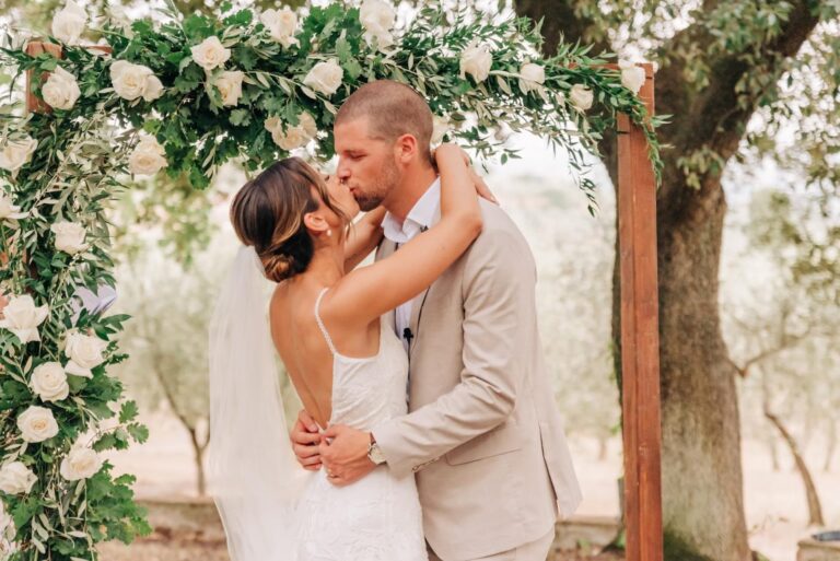 A kiss under an arch of white roses and olive, Umbria Weddings and Events