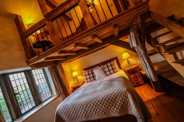 Poirot's Perch, a bedroom under exposed timbers with a stair to a gallery above, Upper House Hayfield