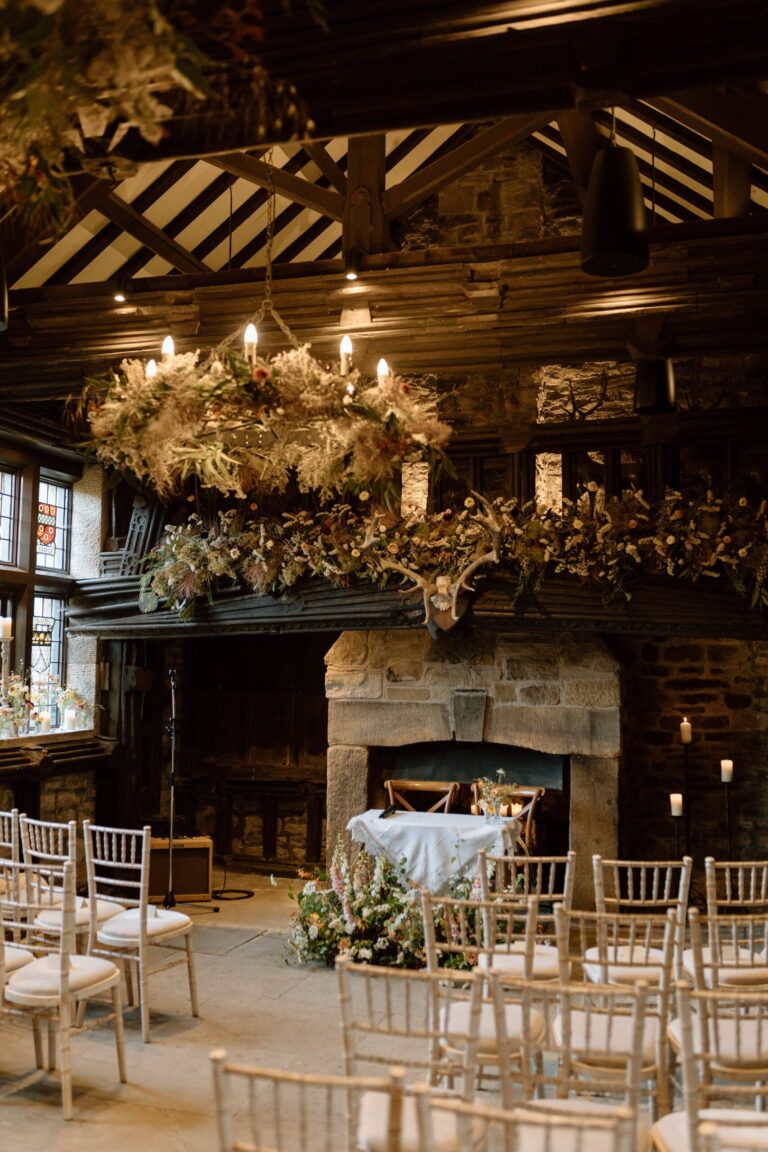 The Great Hall set for a ceremony, with rows of chairs before the stone fireplace and a floral hoop above, Upper House Hayfield