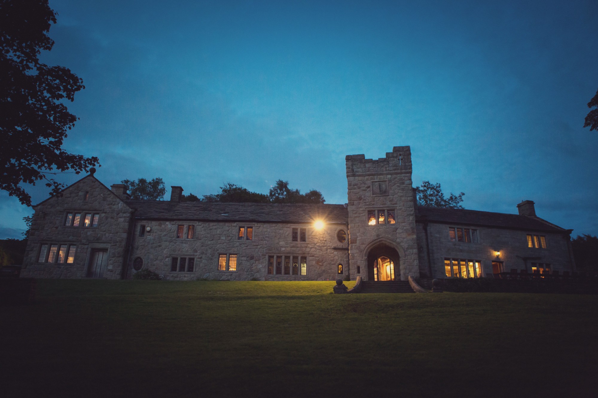 The house and tower at dusk, with lights on in the windows and the front lawn in the foreground, Upper House Hayfield