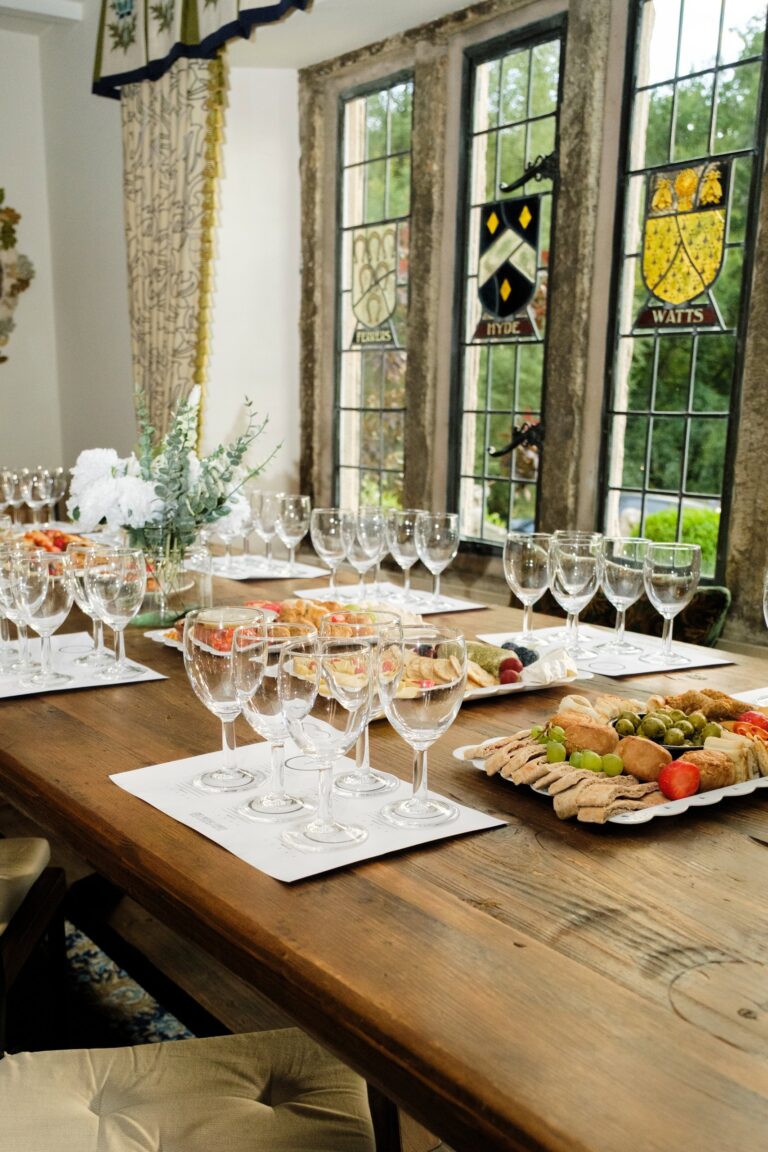 A table laid with glasses and grazing platters beside stained-glass windows bearing family crests, Upper House Hayfield