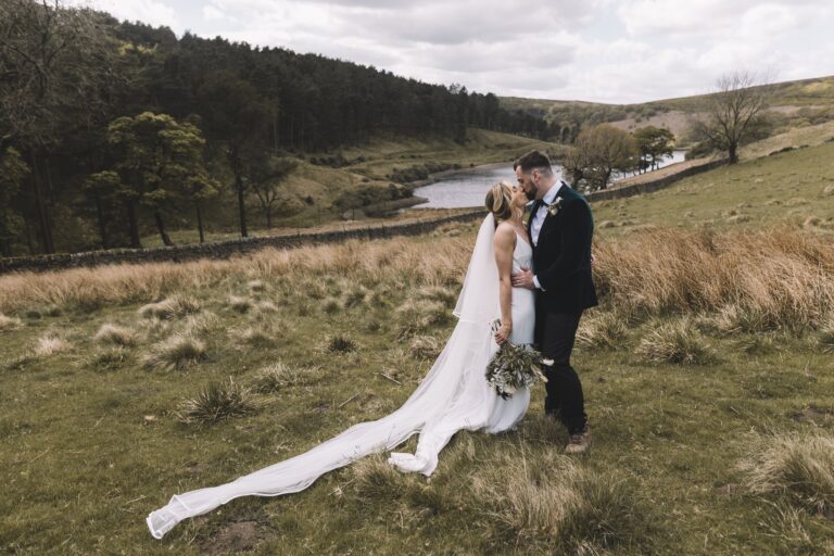 A couple on the open hillside above the reservoir, the bride's veil across the grass, Upper House Hayfield