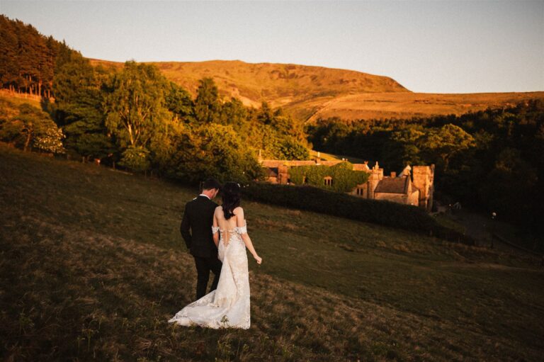 A couple walking across the hillside at sunset towards the house, with the moor lit behind, Upper House Hayfield