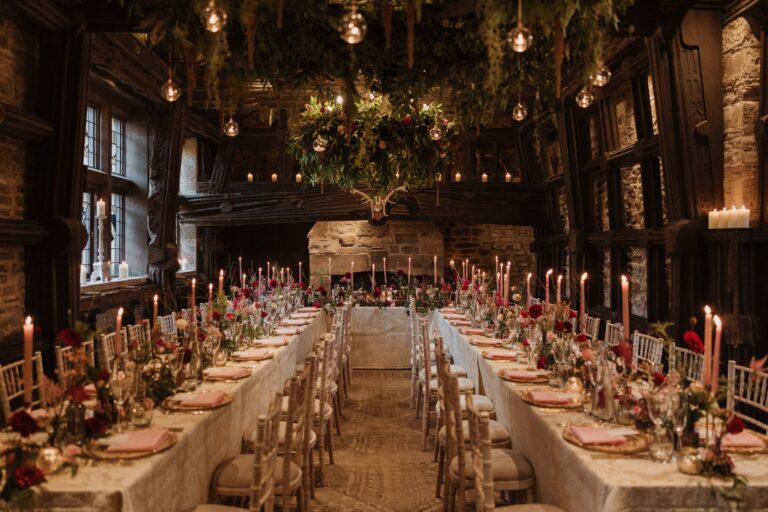 The Medieval Great Hall laid with long candlelit tables, flowers and hanging greenery, Upper House Hayfield