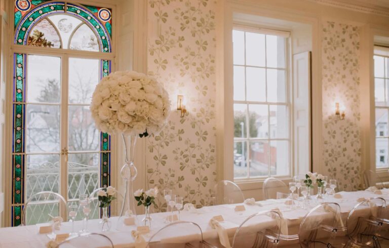 Reception tables laid with tall florals, stained glass behind, Valentines Mansion & Gardens