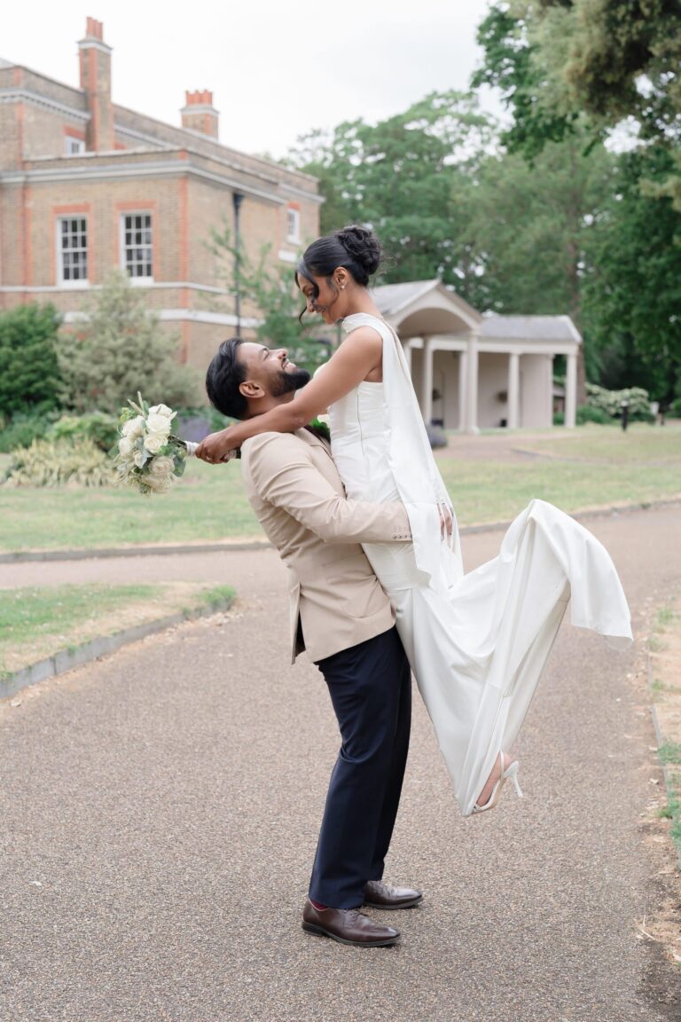 The groom lifting the bride on the drive, mansion and colonnade behind, Valentines Mansion & Gardens