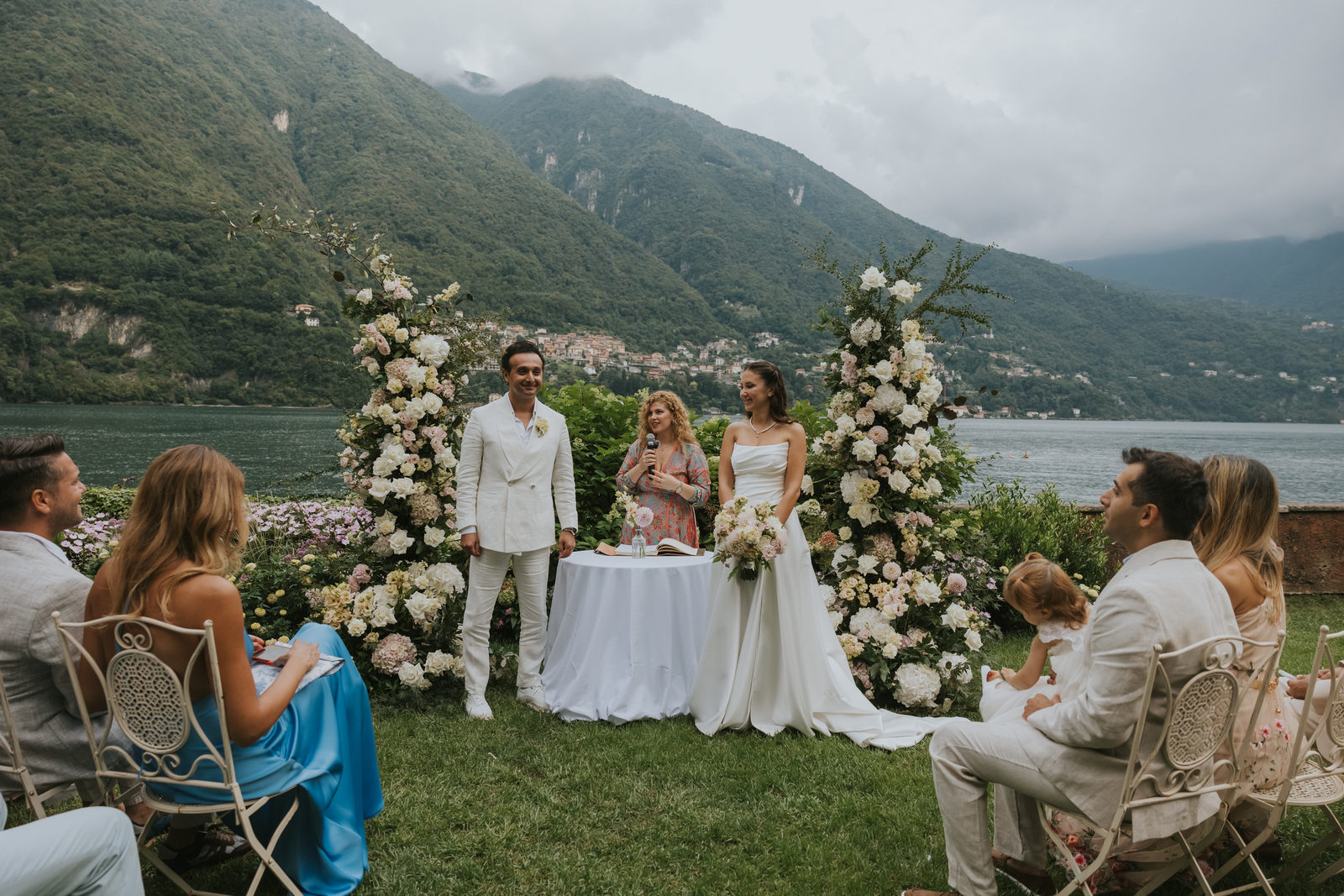 Lake Como ceremony on the lawn with white flower arches and the lake behind, Vera Weddings