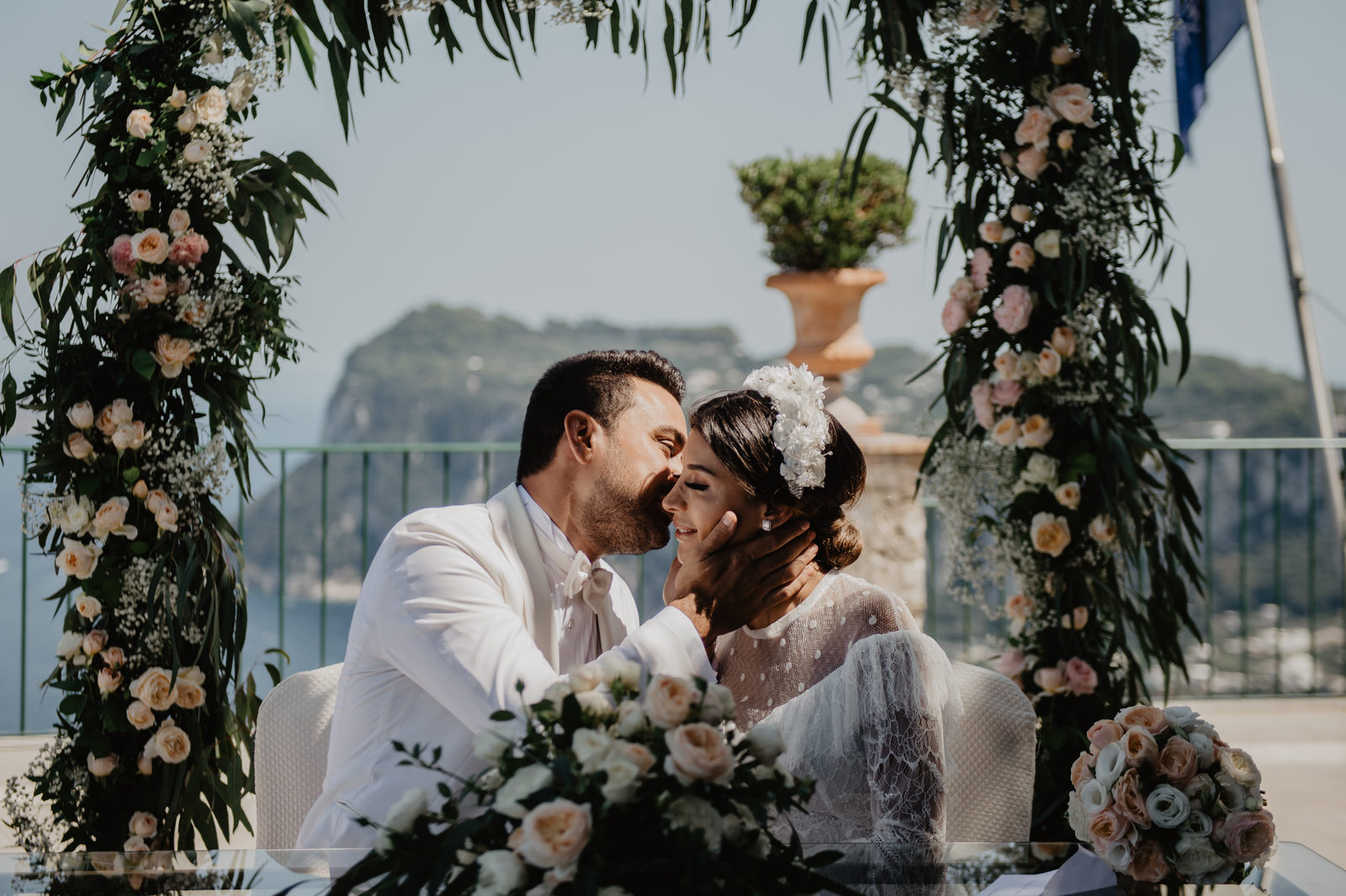 Couple kissing beneath a floral arch on a Capri terrace, Vera Weddings
