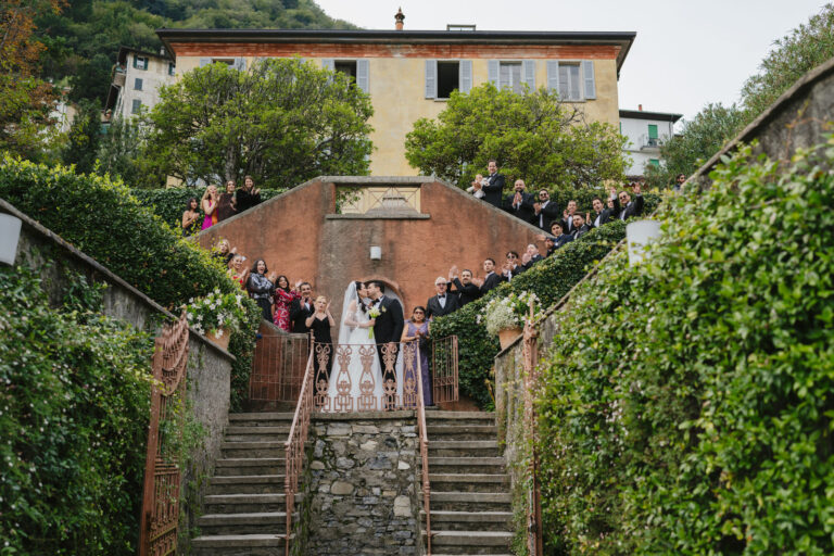 Couple on a stone staircase with guests gathered below, Lake Como, Vera Weddings