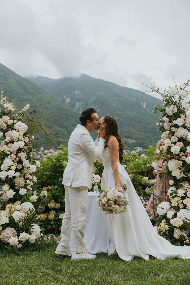 Couple kissing between tall white floral arrangements, Lake Como, Vera Weddings