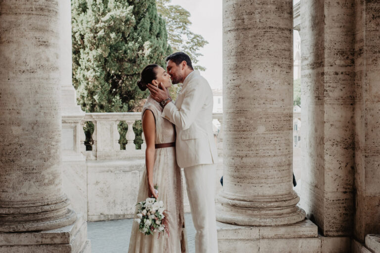 Couple kissing between columns on a Roman terrace, Vera Weddings