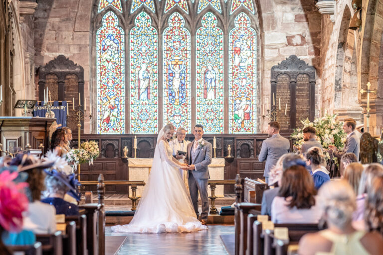 A church ceremony beneath tall stained-glass windows, for a Hawkstone Hall wedding, Shropshire, Victoria Amrose Photography