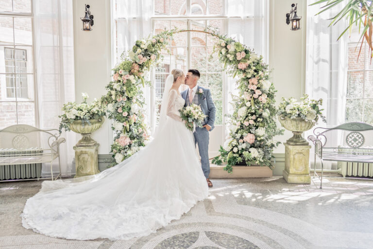 Bride and groom under a floral arch in the conservatory at Hawkstone Hall, Shropshire, Victoria Amrose Photography