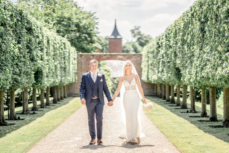 Walking hand in hand down the clipped tree avenue in the walled garden, Combermere Abbey, Shropshire, Victoria Amrose Photography