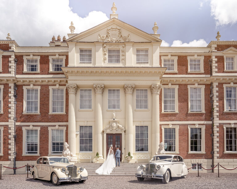 Bride and groom on the forecourt of Hawkstone Hall between two vintage cars, Shropshire, Victoria Amrose Photography