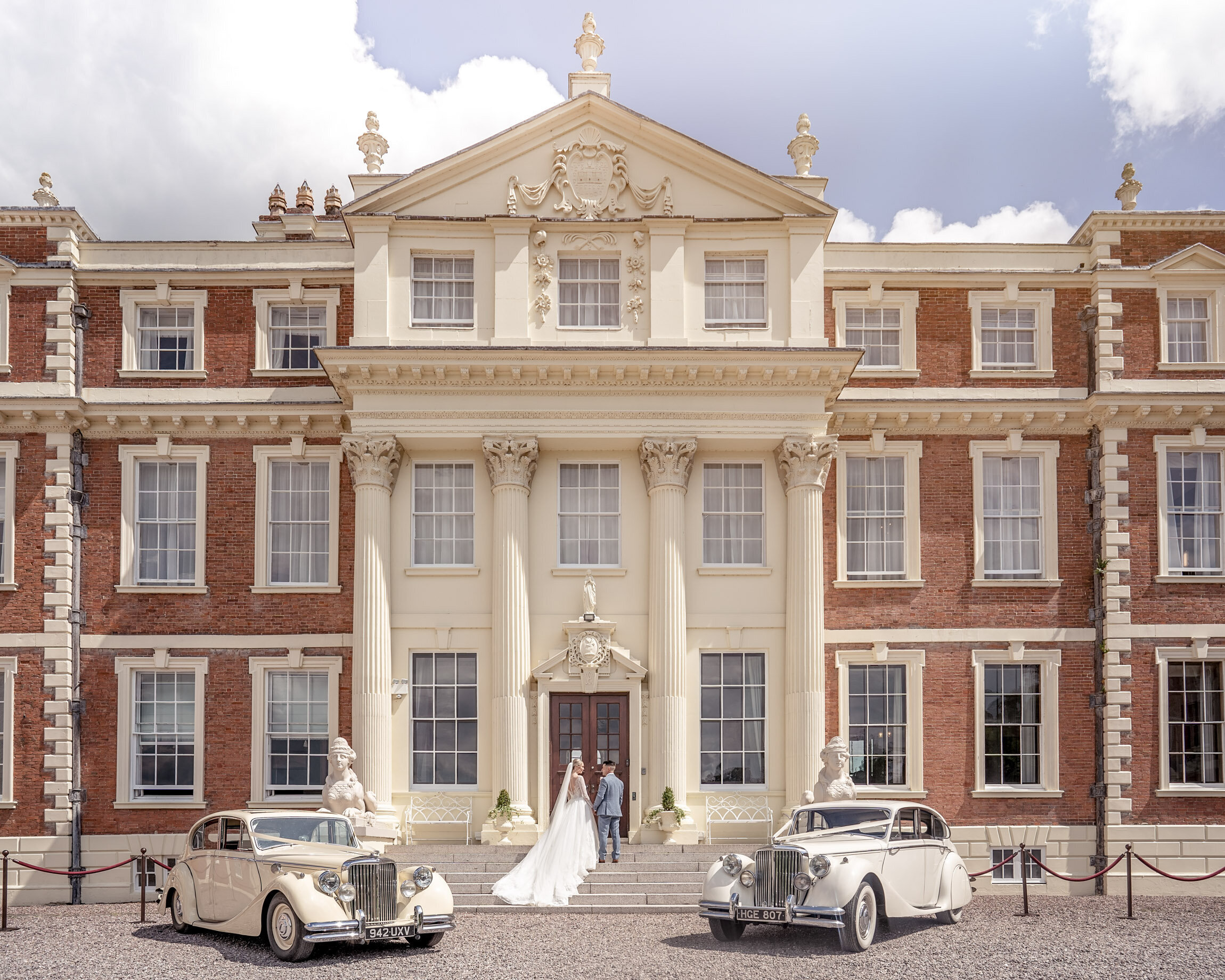 Bride and groom on the forecourt of Hawkstone Hall between two vintage cars, Shropshire, Victoria Amrose Photography
