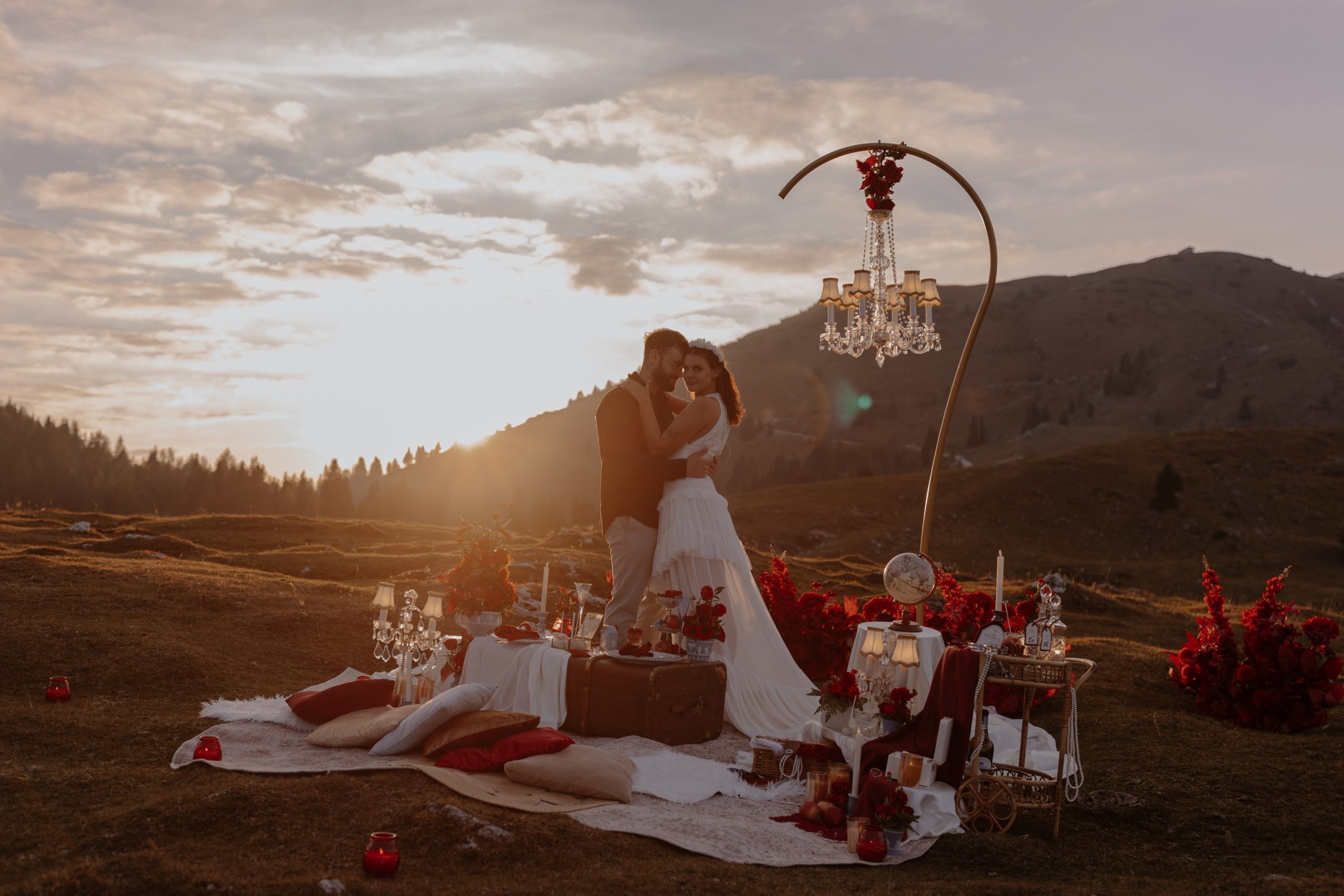 Couple embracing beside a red-rose picnic and chandelier at a mountain sunset, Vienna Picnics
