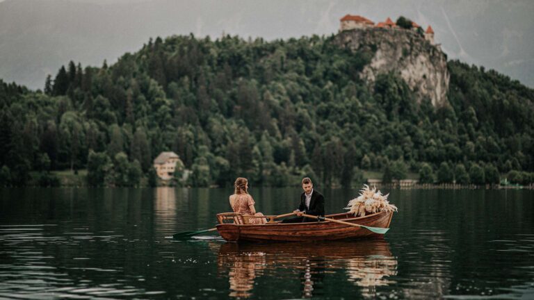 Couple in a wooden rowing boat on the lake, Bled Castle on the hill behind, Vila Bled