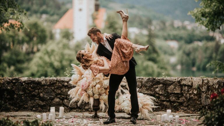 Couple on a stone wall above the lake, with the island church behind, Vila Bled
