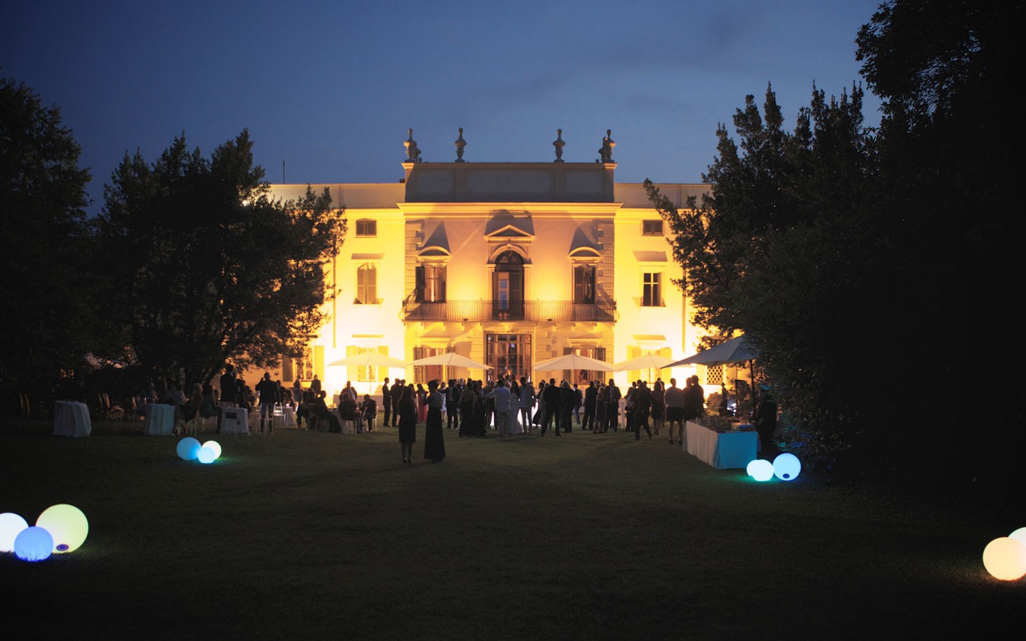 The villa lit at night with guests on the lawn, Villa Mosconi Bertani