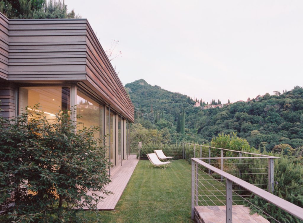 The villa's glazed pavilion and lawn with loungers above the lake