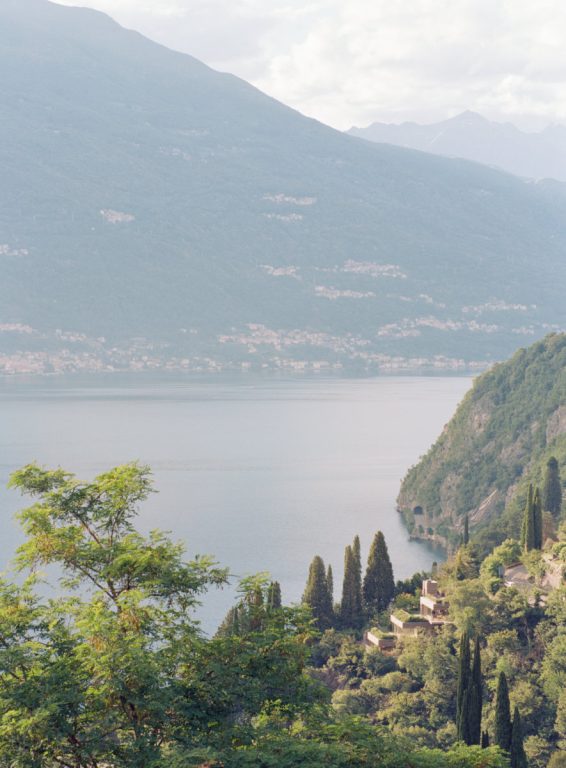 The lake seen from above between the trees, with a cliff and a village on the far shore