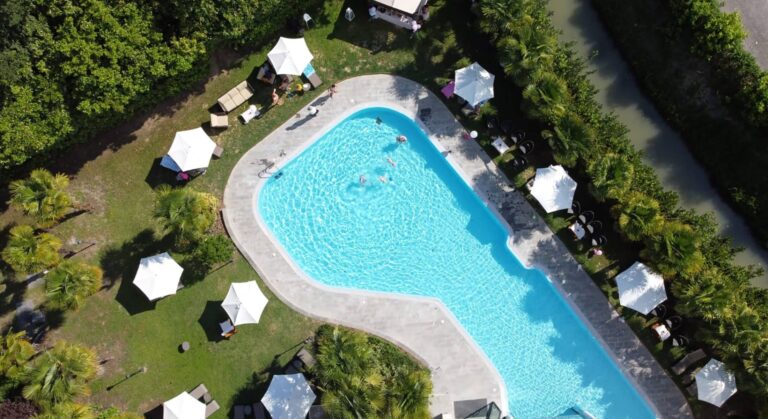 The outdoor swimming pool seen from above, ringed by cabanas and lawn within the wooded park, Villa Pace Park Hotel Bolognese