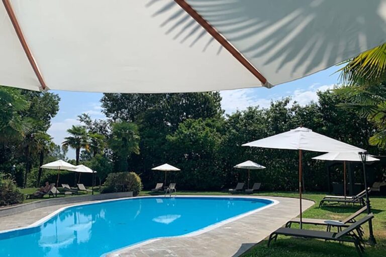 The poolside under white parasols, sun loungers on the grass beneath the trees, Villa Pace Park Hotel Bolognese