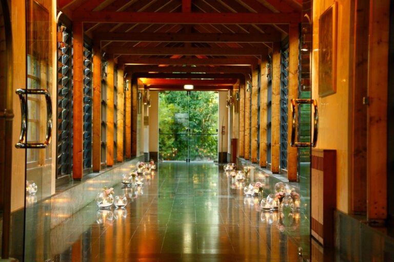 A candlelit passage lined with glass and warm wood, lanterns leading toward the garden, Villa Pace Park Hotel Bolognese