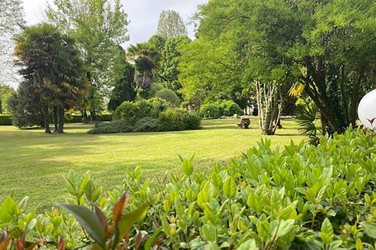 A broad sweep of park lawn edged by a low clipped hedge and mature planting, Villa Pace Park Hotel Bolognese
