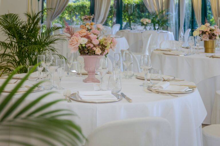 A close view of a wedding table, a blush urn of garden roses among crystal glasses and pale linen, Villa Pace Park Hotel Bolognese
