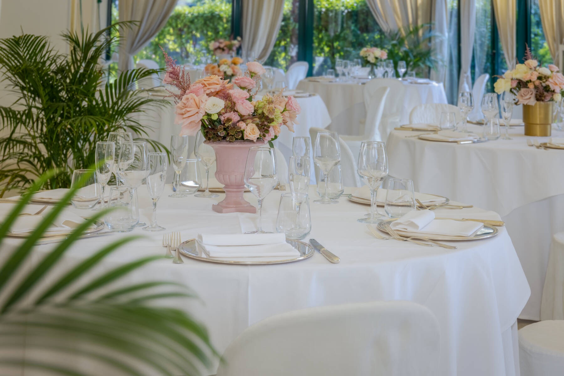 A close view of a wedding table, a blush urn of garden roses among crystal glasses and pale linen, Villa Pace Park Hotel Bolognese