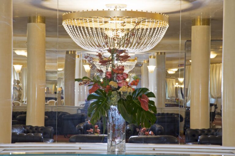 A tall arrangement of anthurium and roses reflected in the mirrored lounge beneath the chandelier, Villa Pace Park Hotel Bolognese