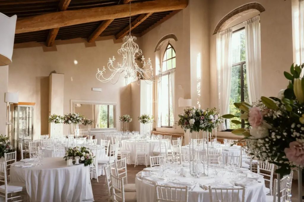 Round tables set with white linen and flowers in a high-ceilinged room with a chandelier