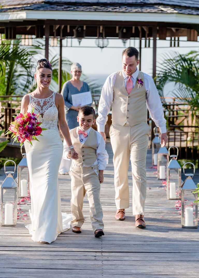 A bride and groom with a young page boy walking along the pool boardwalk lined with lanterns, Villa Susanna St Lucia
