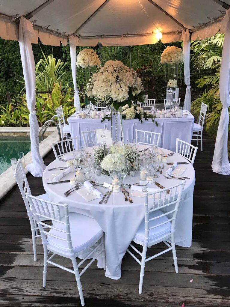 A round table dressed with white flowers and Chiavari chairs under a canopy on the deck, Villa Susanna St Lucia