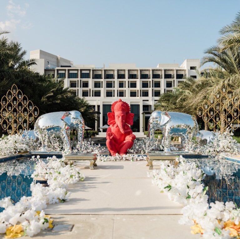 Ceremony aisle lined with white orchids, mirrored elephants and a red Ganesh figure in front of a hotel, Vivaah Weddings