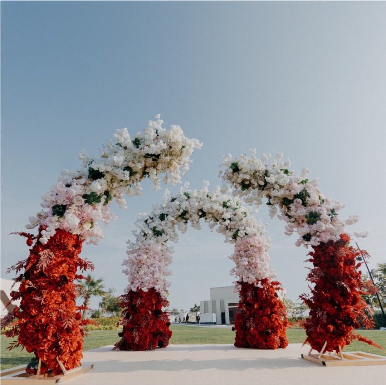 Three arches of white and red flowers in a garden beside the sea, Vivaah Weddings