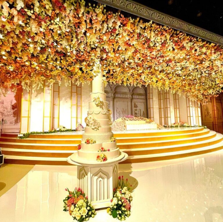 Reception stage with a tiered cake and a wall of flowers, Vivaah Weddings