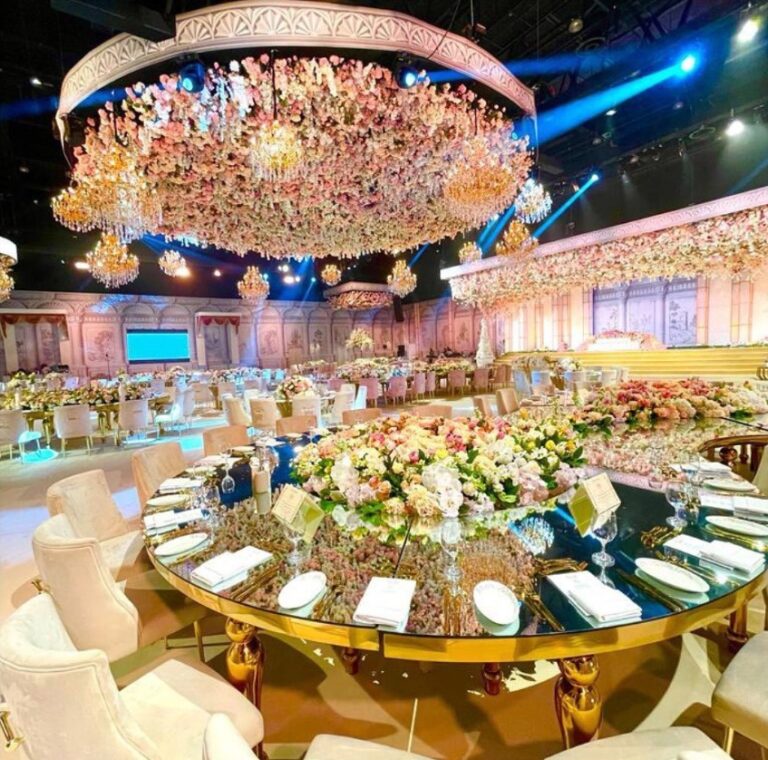 Ballroom with a floral chandelier above round mirrored tables, Vivaah Weddings