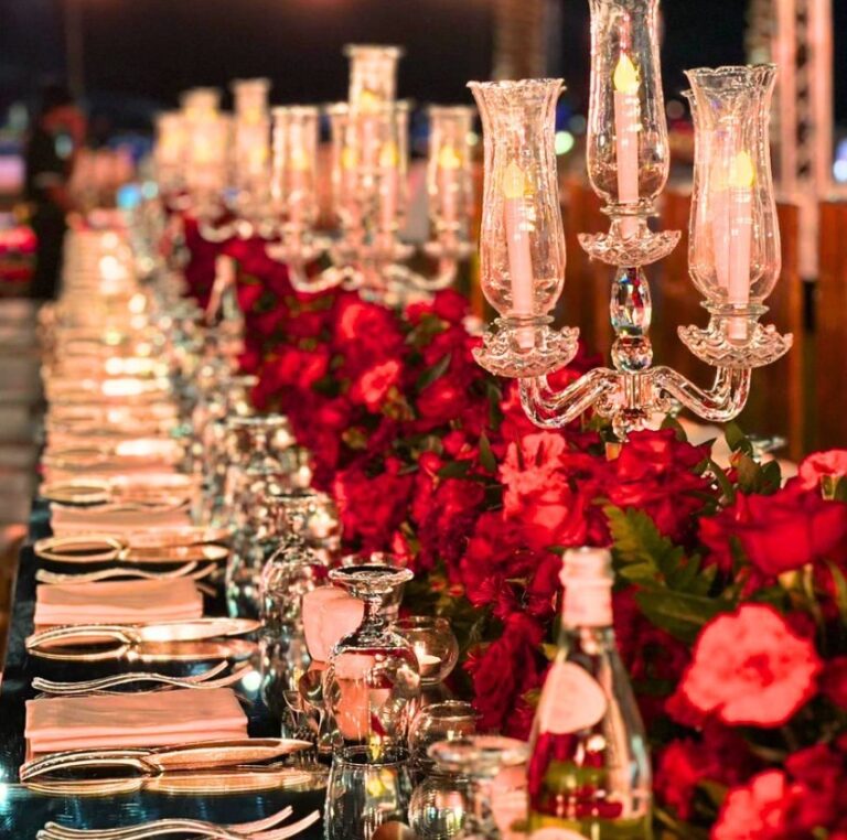 Table of red roses and glass candelabras at an evening reception, Vivaah Weddings