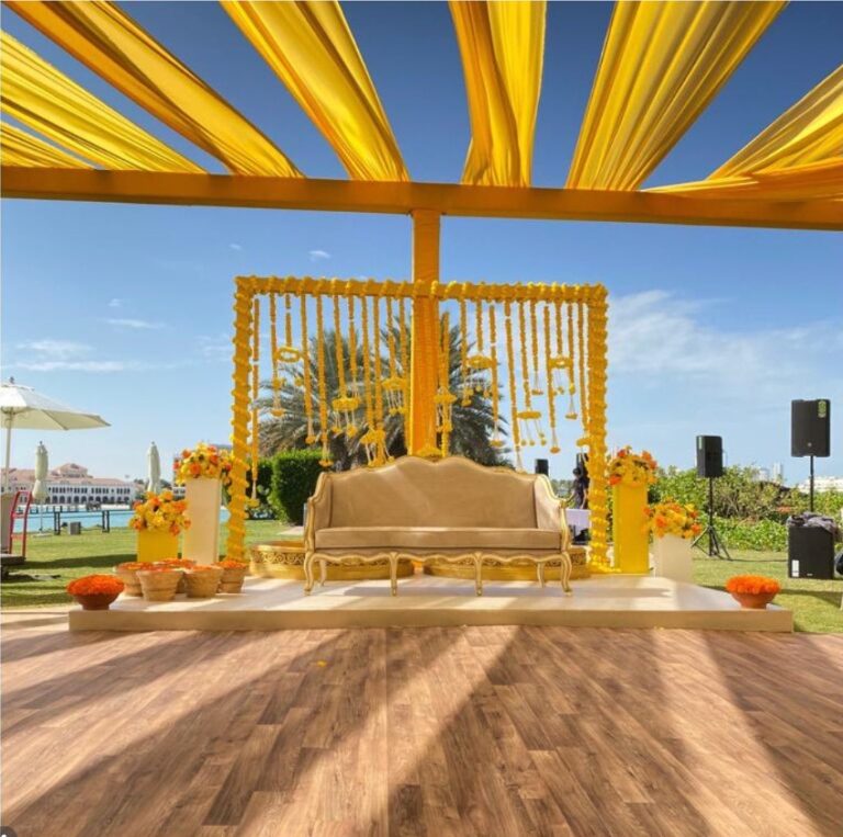 Haldi stage under yellow drapes with a marigold backdrop and a gold sofa, Vivaah Weddings