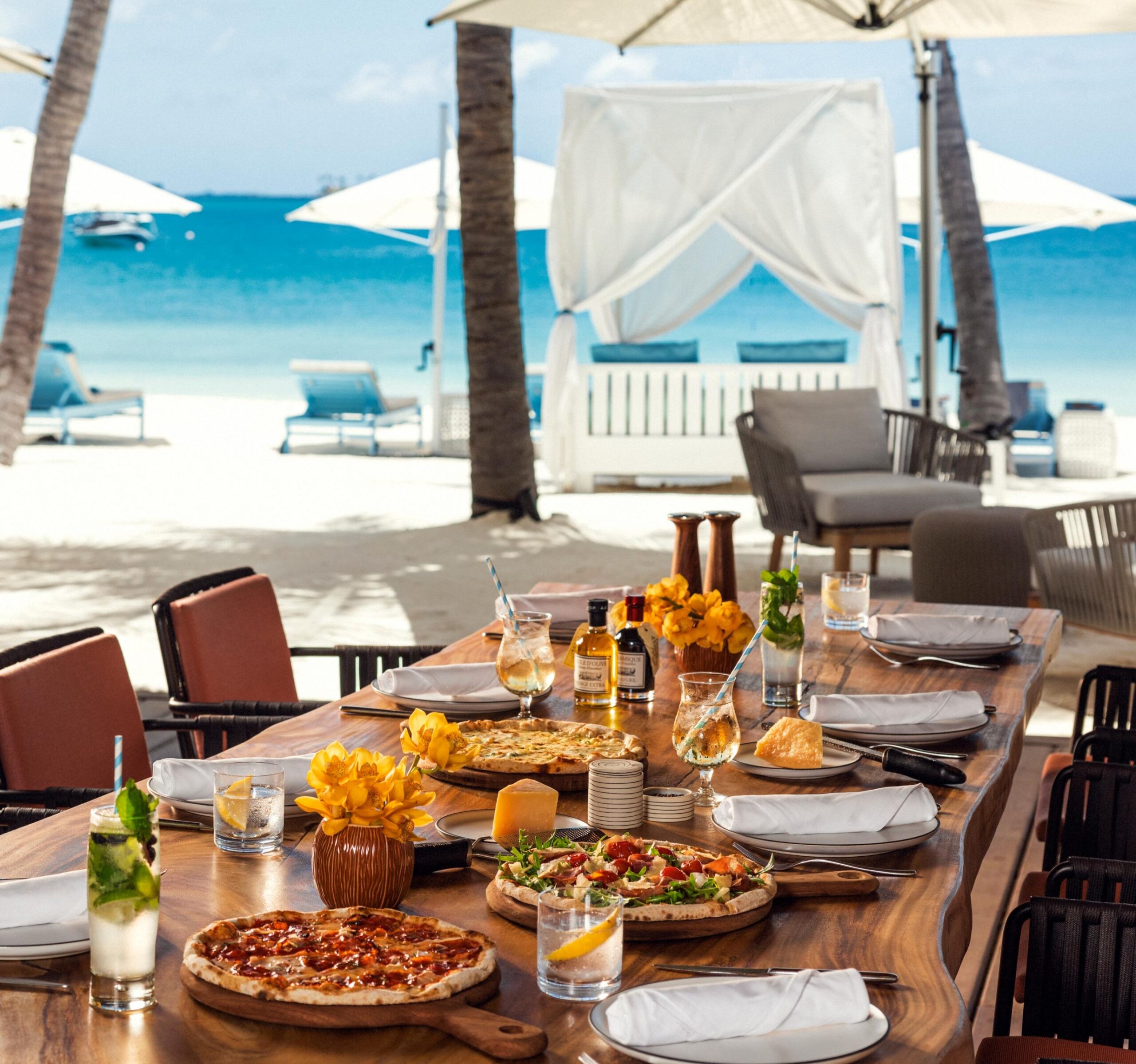 A shared table of dishes beside a beach canopy, Waldorf Astoria Maldives Ithaafushi