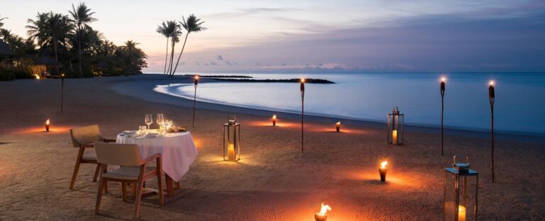 A table for two set on the sand at dusk, Waldorf Astoria Maldives Ithaafushi